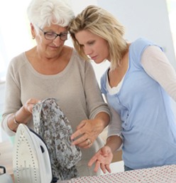 A woman and an older lady ironing clothes.